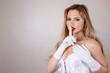 An attractive sexy woman with long blonde hair, red lipstick and white vintage long gloves with a white corset basque lingerie looking sexy and seductive with her finger on her lips