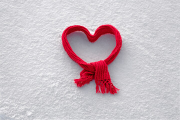 red knitted scarf folded in the shape of a heart on white snow, cute background for valentine's day