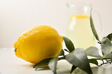 Wall Mural - Lemon and leaves on white table and jug in background