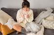 © Antonio Ovejero Diaz/Westend61 - Happy woman having coffee in mug while sitting on sofa at home during winter