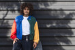 © NOVELLIMAGE/Westend61 - Young man with multi colored jacket standing by skateboard against black wall