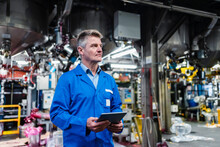 Mature Technician Day Dreaming While Holding Digital Tablet In Factory