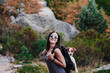 © Eva Blanco/Westend61 - Cheerful woman wearing sunglasses carrying dog in backpack while hiking on mountain