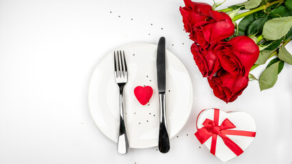 red heart on white plate, gift box, knife and fork on white background. Romantic table setting for Valentines day, holidays. Valentines day menu and dinner concept. top view, flat lay.