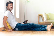 Young Man With Digital Tablet Smiling While Sitting On Floor At Home