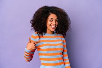 Young african american curly woman isolated on purple background person pointing by hand to a shirt copy space, proud and confident