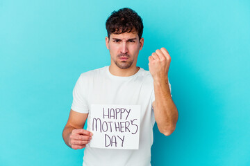 Wall Mural - Young caucasian man holding a happy mothers day placard isolated showing fist to camera, aggressive facial expression.