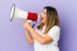 © Asier - Young indian woman holding a megaphone isolated shouting and holding palm near opened mouth.