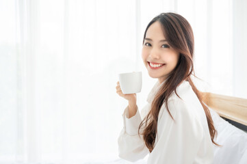 Wall Mural - Young asian woman sitting on bed at home and drinking milk after wake up in the morning