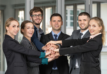 Group portrait of six business people team standing together in an office and stacking their hands together with smile faces and self-confidence. Idea for success of teamwork in modern business