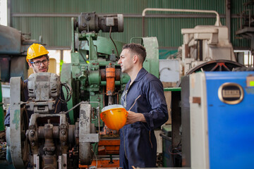 Two workers at an industrial. technician engineer checking process on notebook to machinery in factory. workers using machine equipment in factory