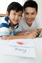 Asian family I love you, dad! Father and son are helping to design a Father's Day card together happily on the bed at home. Concept Greeting card..