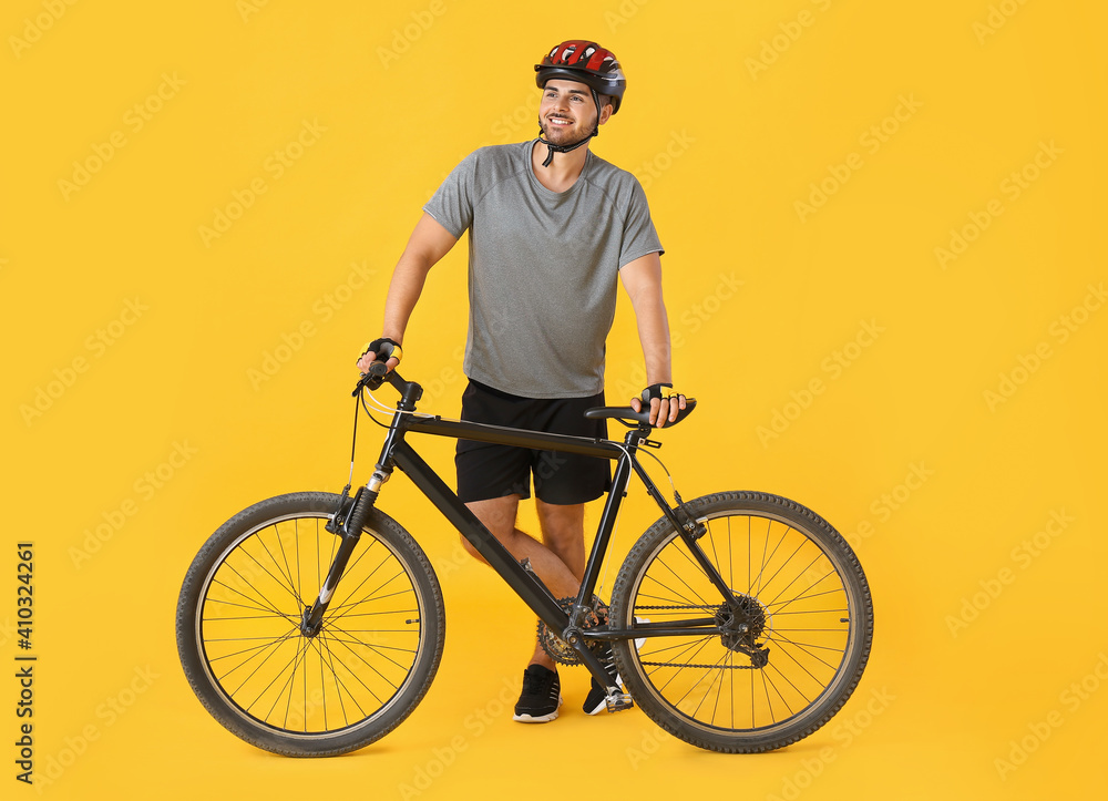 Male cyclist with bicycle on color background
