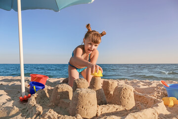 Wall Mural - Little girl playing with sand on sea beach