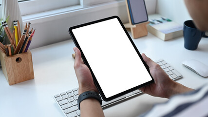 Close up view of young man freelance holding digital tablet with blank screen at home office.