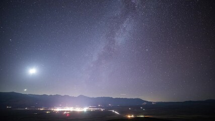 Wall Mural - beautiful time lapse of the stars moving across the night sky. the lights of a small town can be see