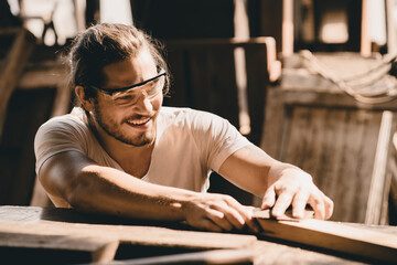 Young Carpenter happy working to making woodcraft furniture in wood workshop look professional high skill real people workman.