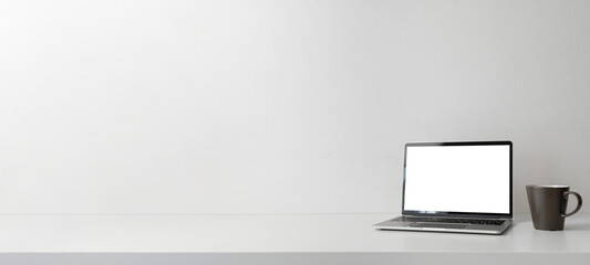 Modern contemporary workspace with blank screen laptop computer and coffee cup on office desk table on white background for copy space. Home office workplace concept.