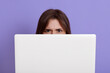© sementsova321 - Model hiding behind laptop isolated over lilac background, having angry facial expression, dark haired female behind white note book, freelancer during work.