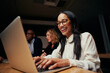 © StratfordProductions - Close-up of successful smiling young African American businesswoman sitting near coworkers using laptop in office