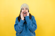 © Irene - Young beautiful woman wearing blue casual sweater and wool hat shouting and screaming loud to side with hands on mouth