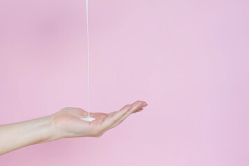 a stream of white cream pours on a woman's hand on a pink background. Skin Care concept. Copy space