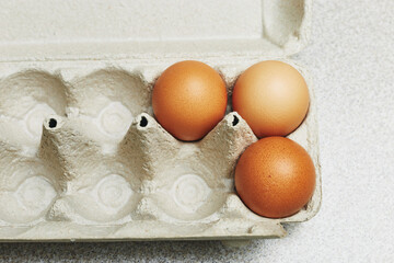 Wall Mural - Culinary class in a kitchen. Three tinted brown chicken eggs in an open carton box on the table ready for cooking. Close-up view.