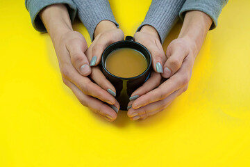 Wall Mural - Hands on a yellow background with coffee, love. Coffee with milk, black cup. Selective focus.