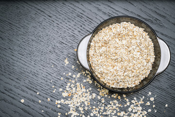 Dry oatmeal porridge in a transparent bowl on a dark background with copy space, top view.