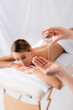 © LIGHTFIELD STUDIOS - masseur holding glass container and pouring oil on hand near woman resting on massage table and blurred background