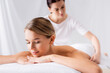 Young woman lying on massage table near masseur on blurred background