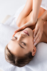 pleased young woman with closed eyes touching face and lying on massage table in spa salon