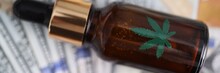 Bottle Of Marijuana Extract Lying On Large Sum Of Dollars Closeup. Illegal Sale Of Drugs Concept