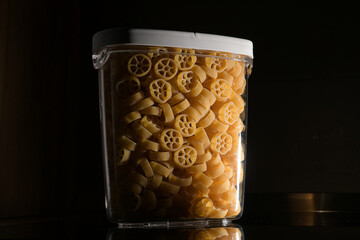 Wall Mural - Close up view of jar full with Rotelle Wagon wheel-shaped pasta against dark background