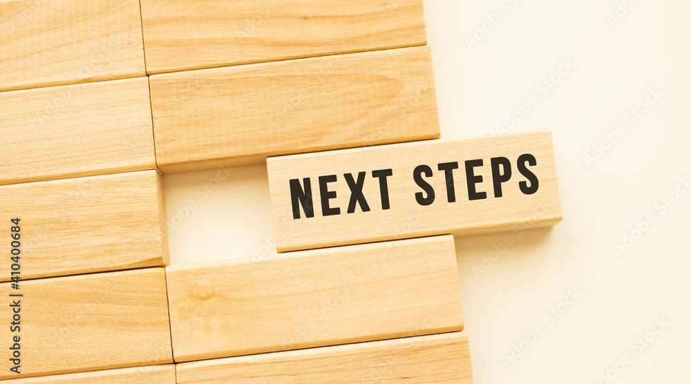 NEXT STEPS text on a strip of wood lying on a white table.