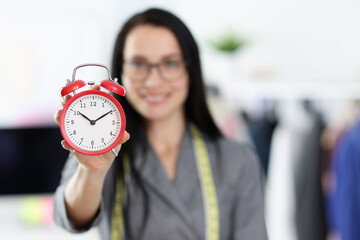 Woman seamstress holding red alarm clock closeup