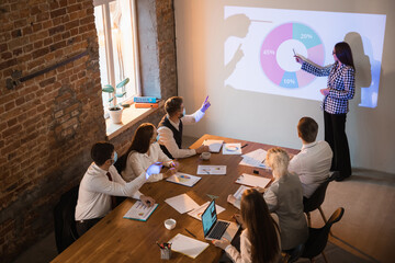 Report. Female speaker giving presentation in hall at university workshop. Audience or conference hall. Co-workers in face masks listening at the table. Scientific, business event, training. High