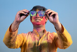 Fototapeta Młodzieżowe - A HAPPY YOUNG MAN SHOWING GOGGLES FILLED WITH HOLI COLOURS	