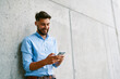 © baranq - Young man texting with mobile phone standing in the city against concrete wall
