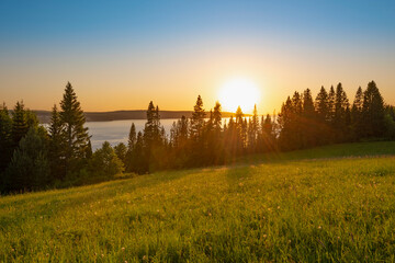 Wall Mural - panoramic view of the kama river from the hill, green meadow, rural road, sunset sky and sun rays.