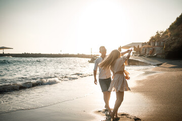 Wall Mural - A couple in love is walking on the beach near the sea. Young family at sunset by the mediterranean sea. Summer vacation concept