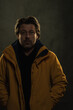© ysbrandcosijn - Shadowy portrait of blonde man in yellow coat in front of grey wall.