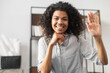 Friendly adorable African American female office worker businesswoman freelancer with Afro hairstyle joyfully waving, smiling and saying hi, making hello sign, greeting and welcoming a newcomer