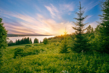 Wall Mural - panoramic view of the kama river from the hill, green meadow, rural road, sunset sky and sun rays.