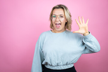 Wall Mural - Young caucasian woman wearing sweatshirt over pink background showing and pointing up with fingers number five while smiling confident and happy