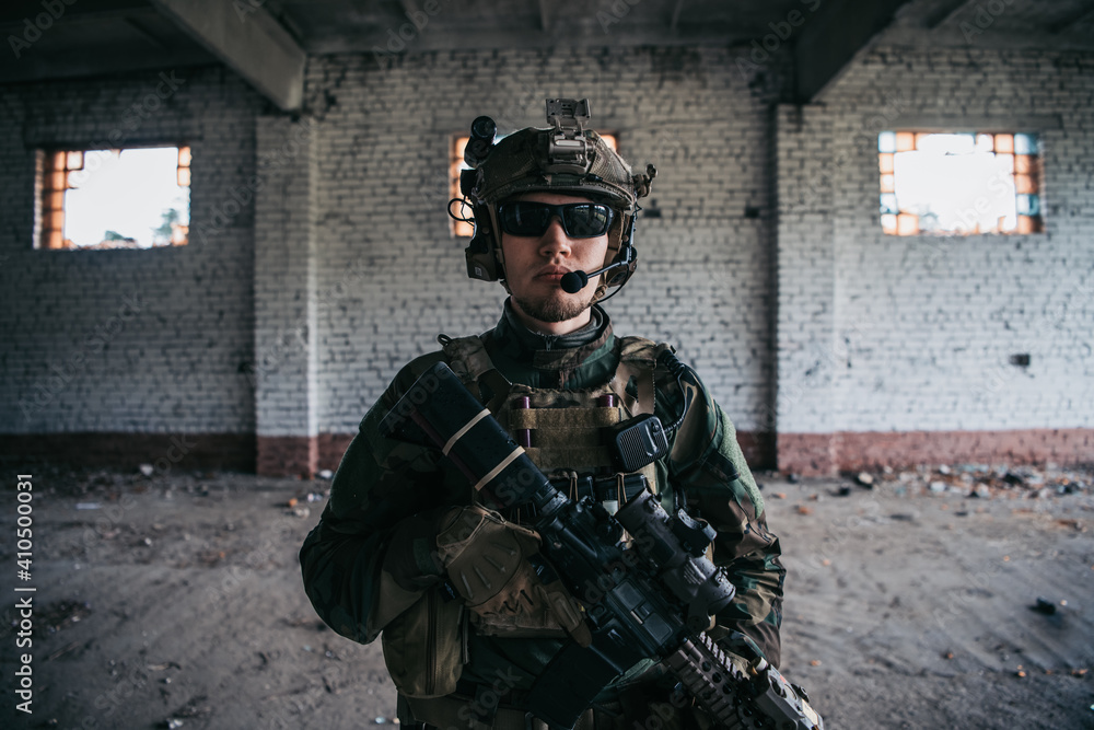 Military man with assault rifle standing inside building, he is ready for combat - obrazy, fototapety, plakaty 
