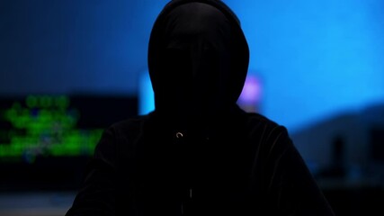 Wall Mural - hacker taking off mask in blue room indoors. unrecognizable man in black hoodie posing. hacking and 