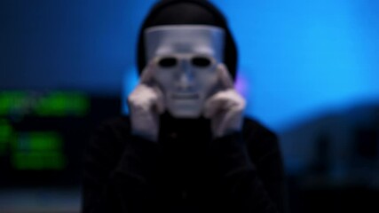 Wall Mural - close-up of white mask in hands white gloves with blurred hacker at background masking. man in black