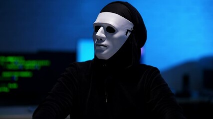 Wall Mural - middle shot of man in black hoodie and anonymous white mask looking around in blue room and typing o
