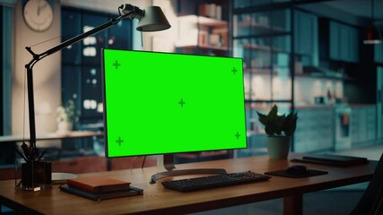Desktop Computer with Mock-up Green Screen Dsiplay Standing on the Wooden Desk in the Creative Cozy Living Room. In the Background Warm Evening Lighting and Open Space Studio with City Window View.